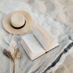 chapéu, livro na areia da praia